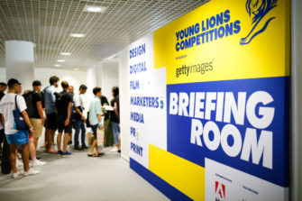 People queuing up next to a yellow and blue board that says Young Lions Competitions